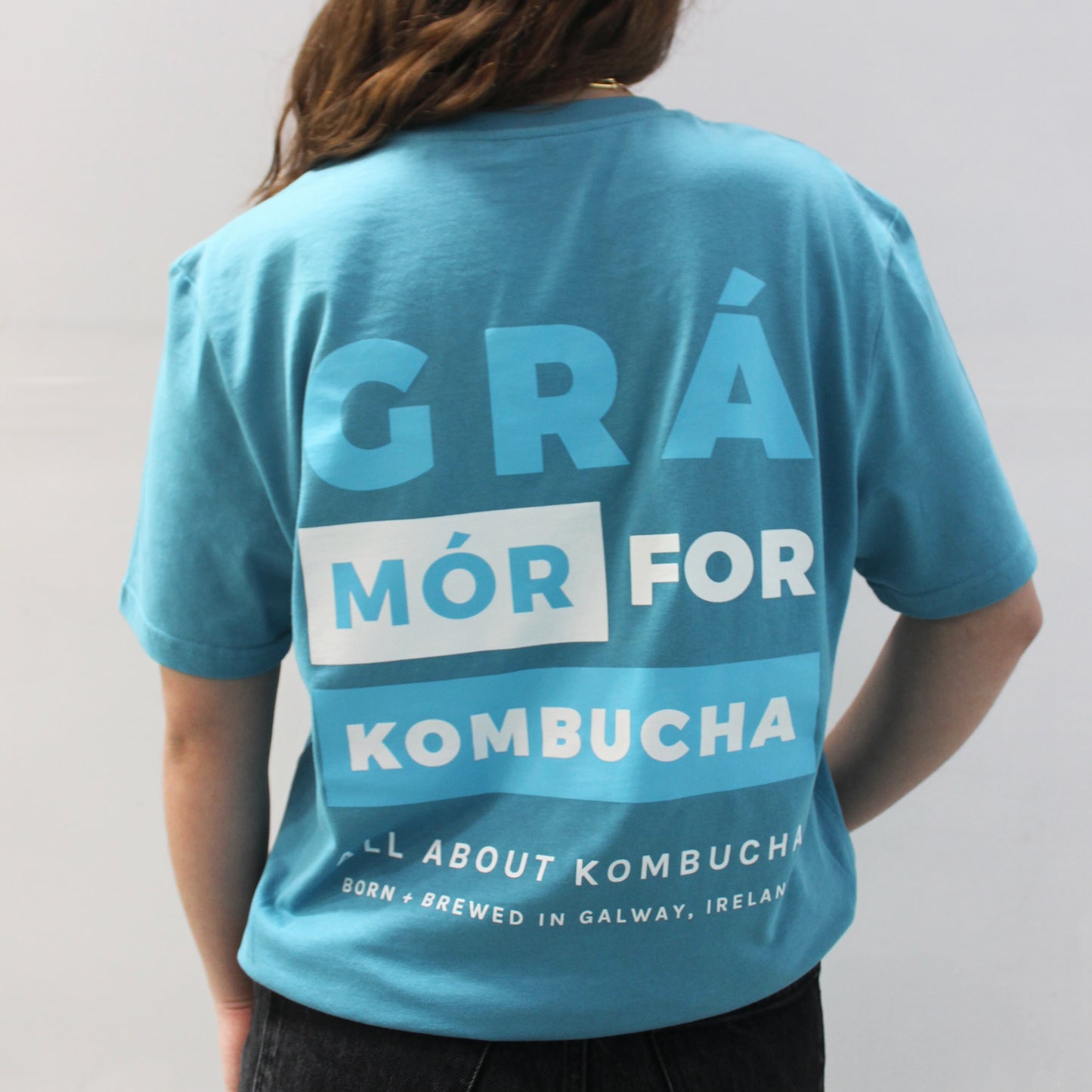 Girl wearing All About Kombucha's branded blue t-shirt with a back that reads 'Grá Mór for Kombucha'