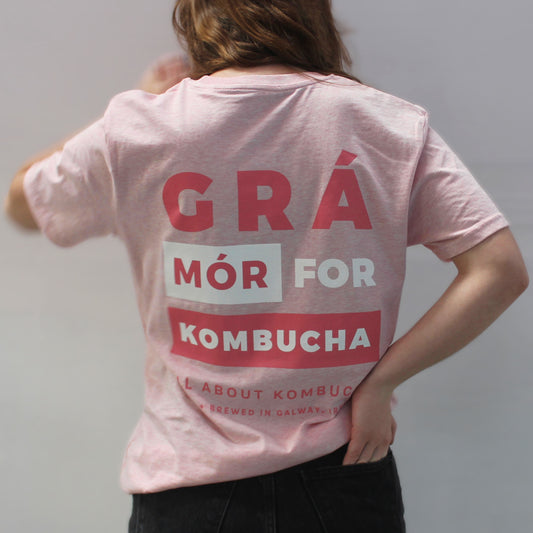Girl wearing All About Kombucha's branded light pink t-shirt with a back that reads 'Grá Mór for Kombucha'